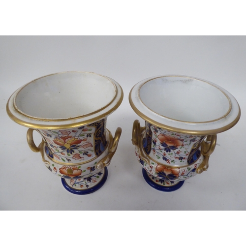 254 - A pair of early 19thC Derby porcelain, twin handled, pedestal urns, decorated in a version of an Ima... 