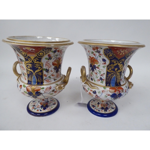 254 - A pair of early 19thC Derby porcelain, twin handled, pedestal urns, decorated in a version of an Ima... 