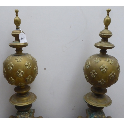 117 - A pair of 19thC Continental brass andirons, each comprising an orb and finial, over a female maskhea... 