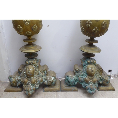 117 - A pair of 19thC Continental brass andirons, each comprising an orb and finial, over a female maskhea... 