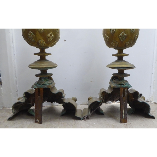 117 - A pair of 19thC Continental brass andirons, each comprising an orb and finial, over a female maskhea... 