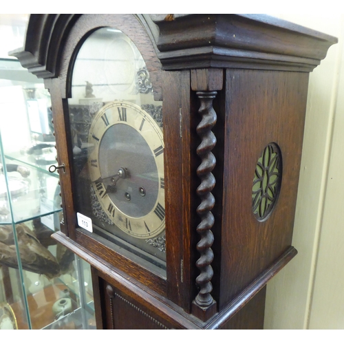 113 - An early 20thC oak cased granddaughter clock, the arched hood decorated with barleytwist columns, th... 