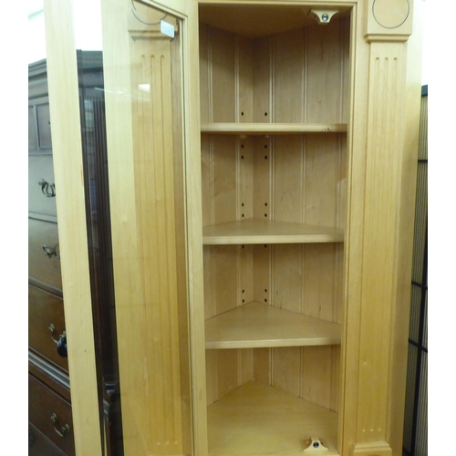 386 - A modern beech two part corner unit, the superstructure with a glazed door and three shelves, over a... 