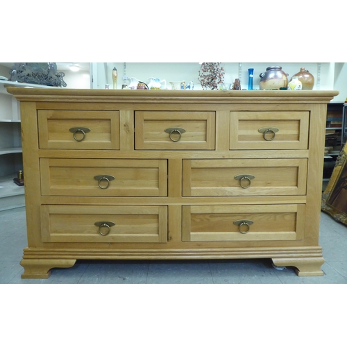 58 - A modern light oak dresser, comprising an arrangement of seven drawers with brass ring handles, rais... 