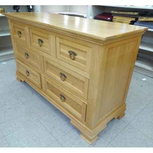 58 - A modern light oak dresser, comprising an arrangement of seven drawers with brass ring handles, rais... 