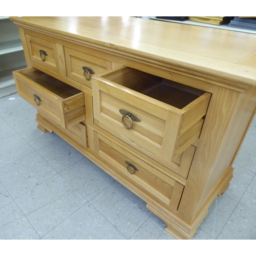 58 - A modern light oak dresser, comprising an arrangement of seven drawers with brass ring handles, rais... 