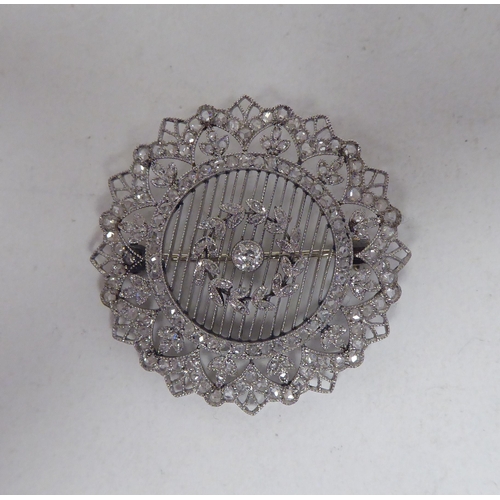 124 - A white metal wire and filigree style diamond set, circular and foliate design brooch