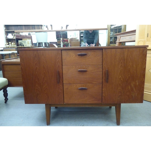 174 - A 1970s teak sideboard, comprising three offset short drawers, flanked by a pair of cupboard doors w... 