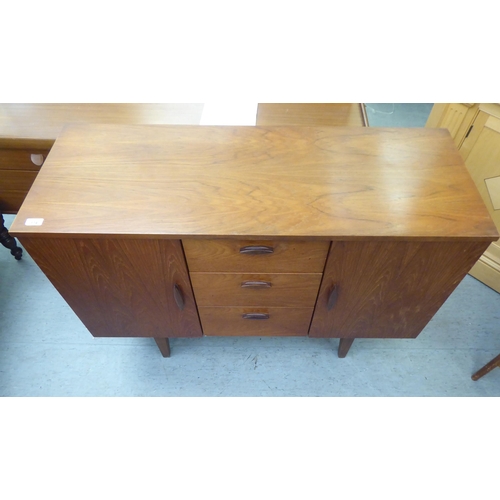 174 - A 1970s teak sideboard, comprising three offset short drawers, flanked by a pair of cupboard doors w... 