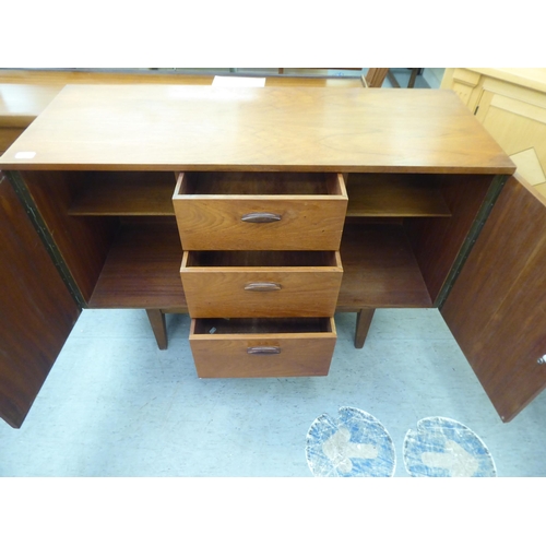 174 - A 1970s teak sideboard, comprising three offset short drawers, flanked by a pair of cupboard doors w... 