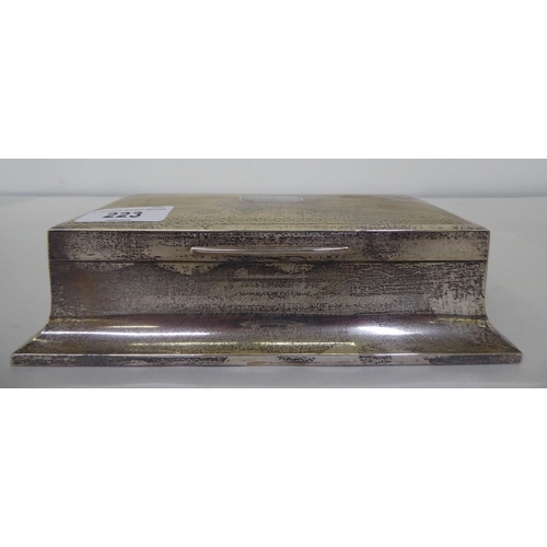 223 - A silver cigarette box of sarcophagus form with engine turned decoration on the hinged lid, enclosin... 