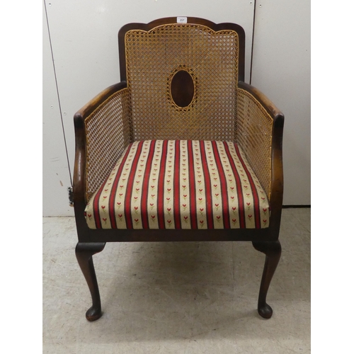 257 - An Edwardian mahogany framed bergere style, enclosed arm chair with woven cane panels, raised on cab... 