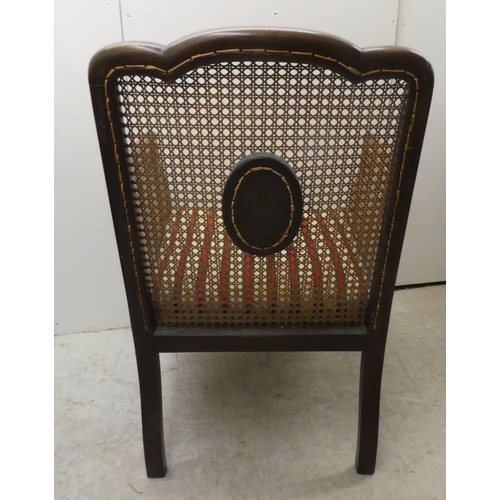 257 - An Edwardian mahogany framed bergere style, enclosed arm chair with woven cane panels, raised on cab... 