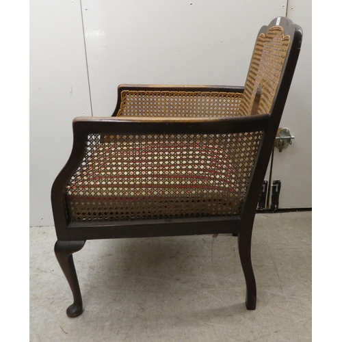 257 - An Edwardian mahogany framed bergere style, enclosed arm chair with woven cane panels, raised on cab... 