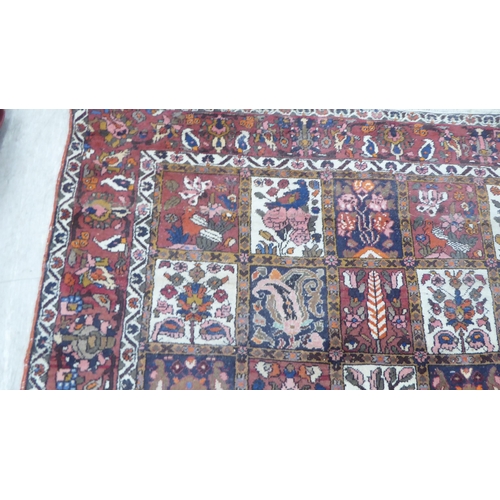 42 - A Persian rug, decorated with symmetrical, repeating floral designs, on a red ground  90