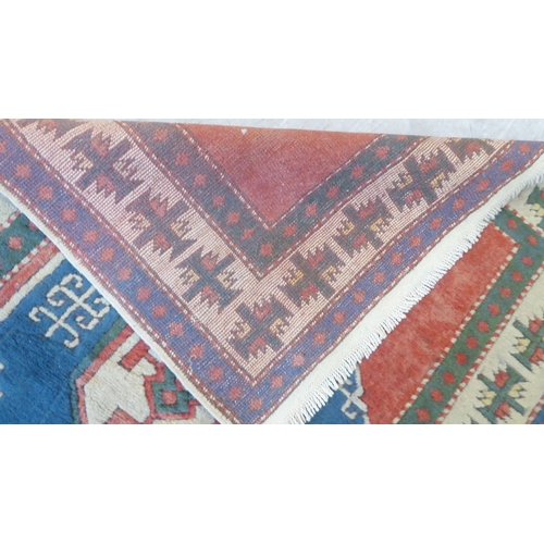 82 - A North African rug, decorated with a central motif, bordered by stylised designs, on a multi-colour... 