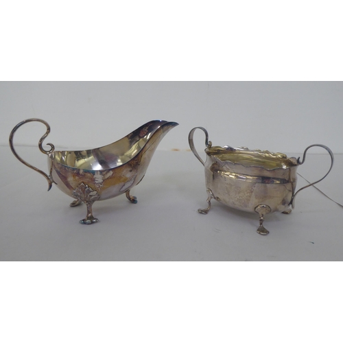 153 - A silver sauce boat with a scrolled handle and a silver, oval twin handled sugar basin  mixed marks