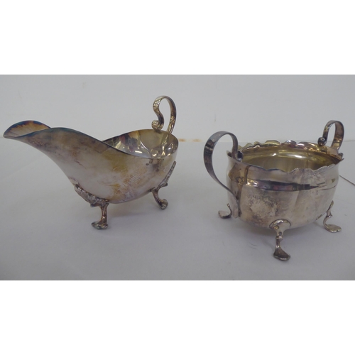 153 - A silver sauce boat with a scrolled handle and a silver, oval twin handled sugar basin  mixed marks