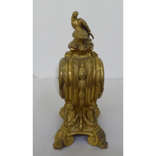 189 - A reproduction of a 19thC gilt metal cased mantel clock of balloon design, surmounted by a pair of d... 