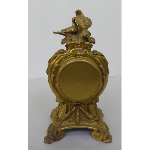 189 - A reproduction of a 19thC gilt metal cased mantel clock of balloon design, surmounted by a pair of d... 