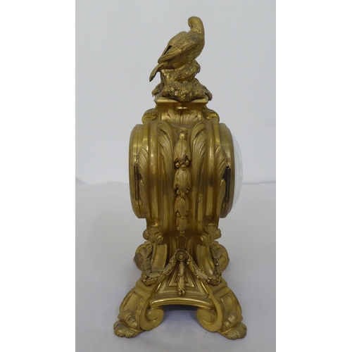 189 - A reproduction of a 19thC gilt metal cased mantel clock of balloon design, surmounted by a pair of d... 