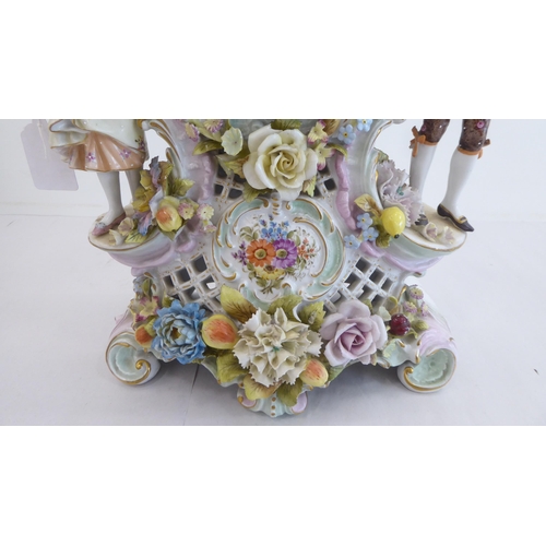 191 - A late 19thC Continental porcelain mantel clock, encrusted with flowers and fruit, surmounted by a m... 