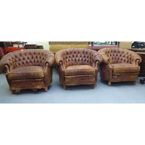 299 - A set of three early/mid 20thC stud and part button upholstered simulated brown hide armchairs, rais... 