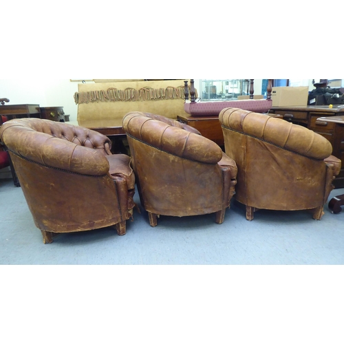 299 - A set of three early/mid 20thC stud and part button upholstered simulated brown hide armchairs, rais... 