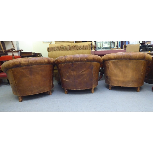 299 - A set of three early/mid 20thC stud and part button upholstered simulated brown hide armchairs, rais... 