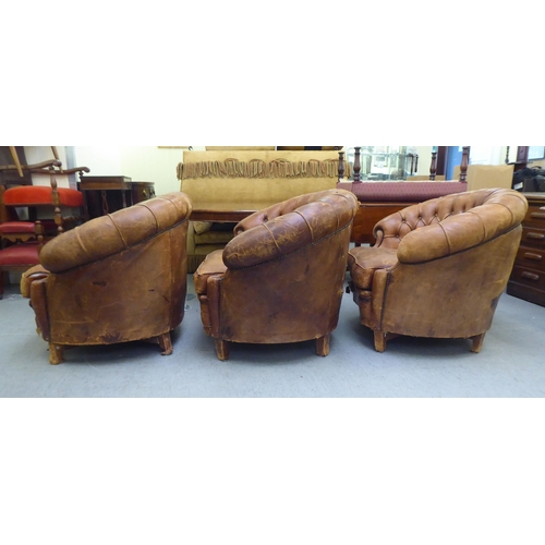 299 - A set of three early/mid 20thC stud and part button upholstered simulated brown hide armchairs, rais... 