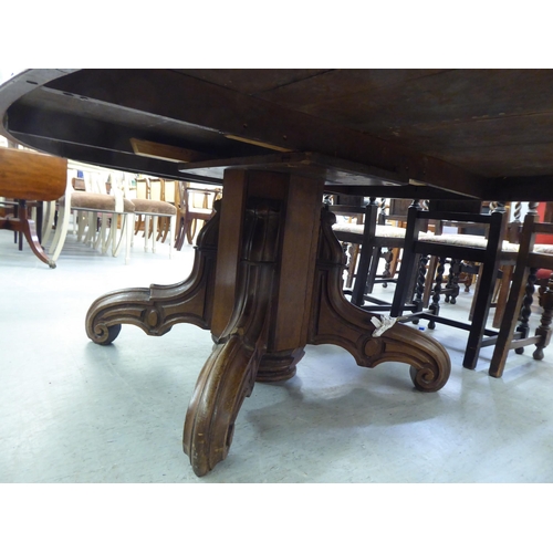 304 - An early 20thC oak pedestal table, the oval planked top raised on a carved C-scroll quadruped base&n... 