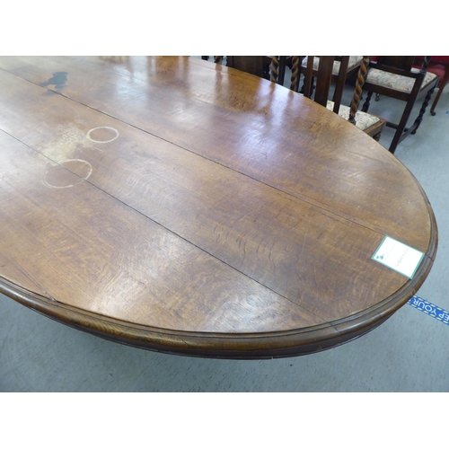 304 - An early 20thC oak pedestal table, the oval planked top raised on a carved C-scroll quadruped base&n... 