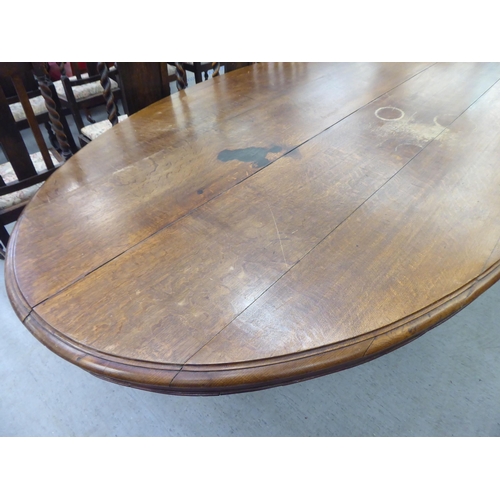 304 - An early 20thC oak pedestal table, the oval planked top raised on a carved C-scroll quadruped base&n... 