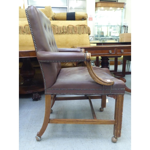 323 - A mid 20thC library style desk chair, part button upholstered in brown hide, raised on square forele... 