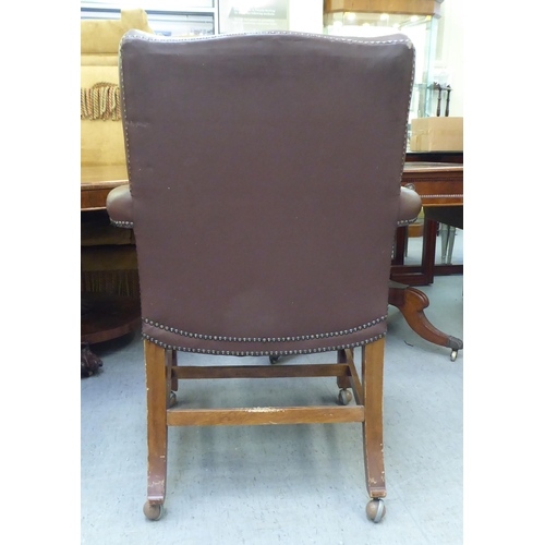 323 - A mid 20thC library style desk chair, part button upholstered in brown hide, raised on square forele... 