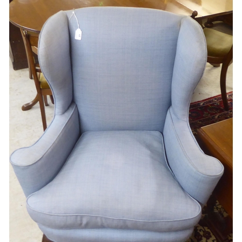 68 - An early 20thC Georgian style and later fabric upholstered, wingback enclosed armchair, raised on st... 