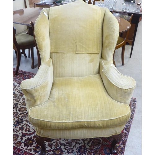 71 - An early 20thC Georgian style and later fabric upholstered, wingback, enclosed armchair, raised on C... 