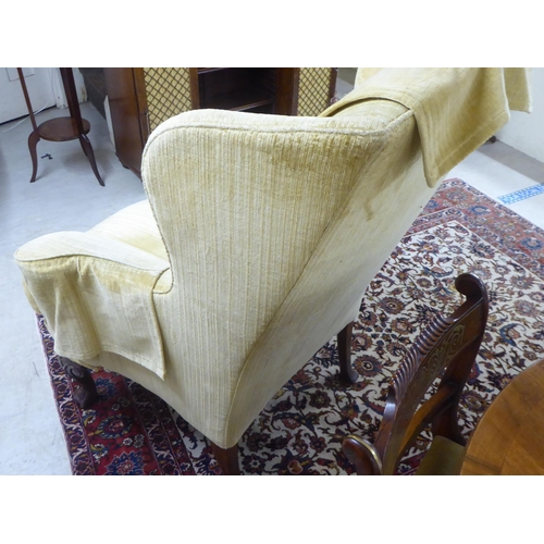 71 - An early 20thC Georgian style and later fabric upholstered, wingback, enclosed armchair, raised on C... 