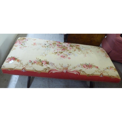 81 - A 20thC long stool with a floral patterned fabric, cushioned top, raised on X-design ends, united by... 