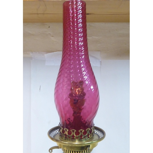 149 - An early 20thC pale green china and brass mounted table pedestal lamp with a cranberry coloured glas... 