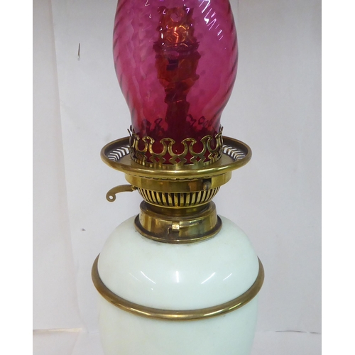 149 - An early 20thC pale green china and brass mounted table pedestal lamp with a cranberry coloured glas... 