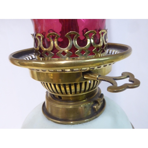 149 - An early 20thC pale green china and brass mounted table pedestal lamp with a cranberry coloured glas... 
