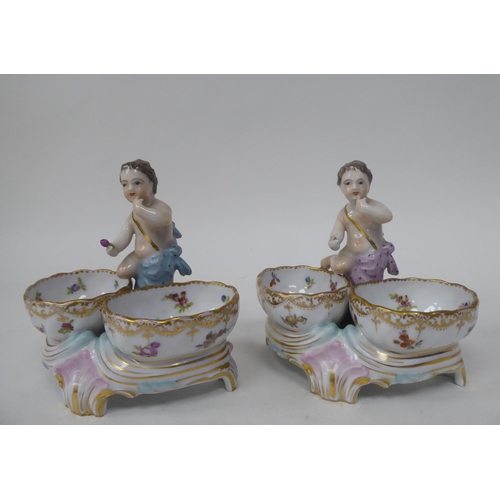 92 - A pair of 20thC Dresden porcelain double salt cellars, featuring a cherubic figure with floral decor... 