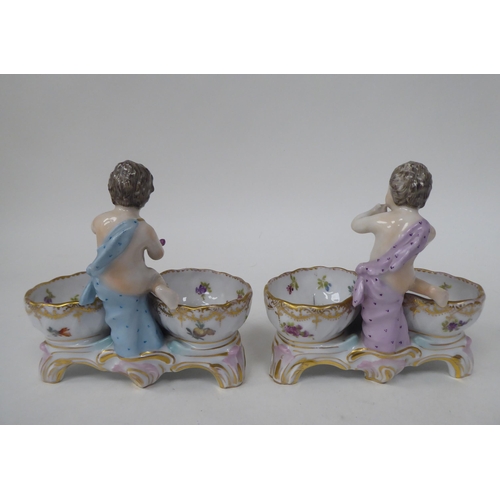 92 - A pair of 20thC Dresden porcelain double salt cellars, featuring a cherubic figure with floral decor... 