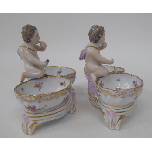 92 - A pair of 20thC Dresden porcelain double salt cellars, featuring a cherubic figure with floral decor... 