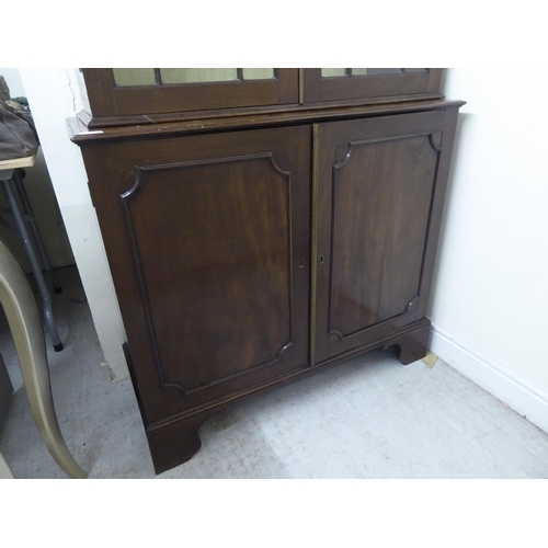 176 - A Regency style two part mahogany cabinet bookcase with a straight cornice, over a pair of astragal ... 