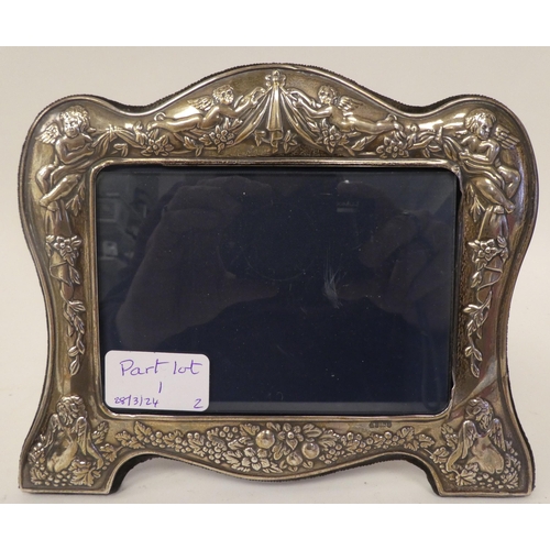 1 - Two dissimilar, glazed, silver mounted photograph frames with embossed ornament, fabric backs and ea... 