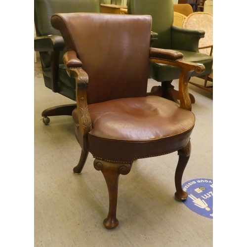 185 - An early 20thC mahogany framed desk chair with a brown hide upholstered back and seat, raised on cab... 