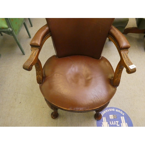 185 - An early 20thC mahogany framed desk chair with a brown hide upholstered back and seat, raised on cab... 