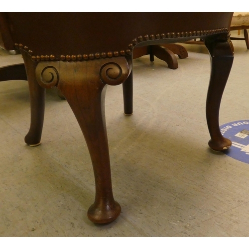 185 - An early 20thC mahogany framed desk chair with a brown hide upholstered back and seat, raised on cab... 